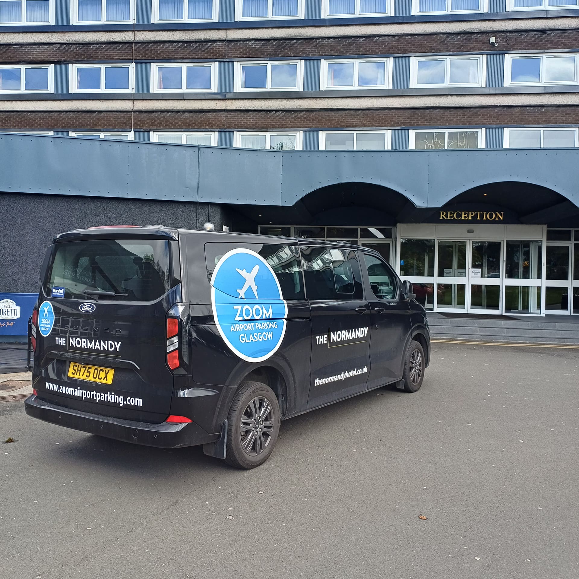 Zoom Airport Parking Glasgow shuttle minibus parked directly outside the main entrance reception of The Normandy Hotel in Renfrew.