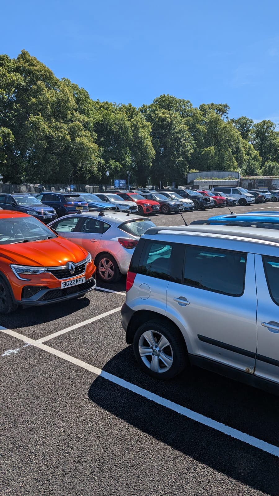 Secure off-site airport parking at Zoom Airport Parking Glasgow facility, featuring parked cars on a clean tarmac lot surrounded by high security fencing and trees under a clear blue sky.